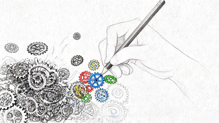 A pencil held by a hand drawing a complex system of gears on a white paper background.